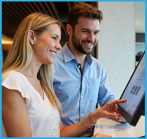 Happy couple checking into a hotel using a self-service kiosk from logic controls.